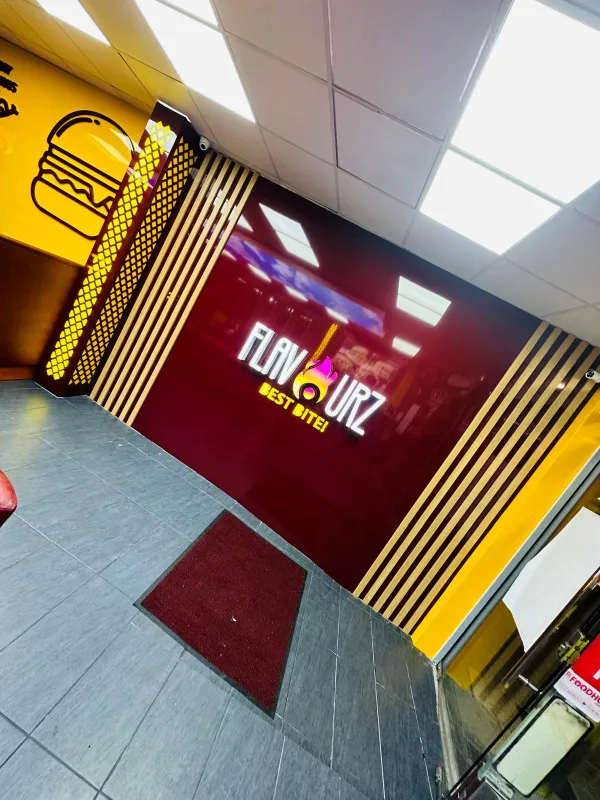 Restaurant branding with an illuminated 3D logo sign on a maroon feature wall, wood slat panels and yellow burger graphics