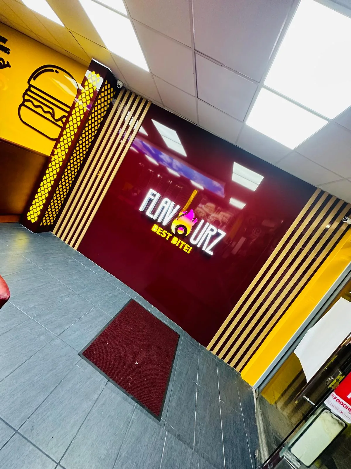 Restaurant branding with an illuminated 3D logo sign on a maroon feature wall, wood slat panels and yellow burger graphics