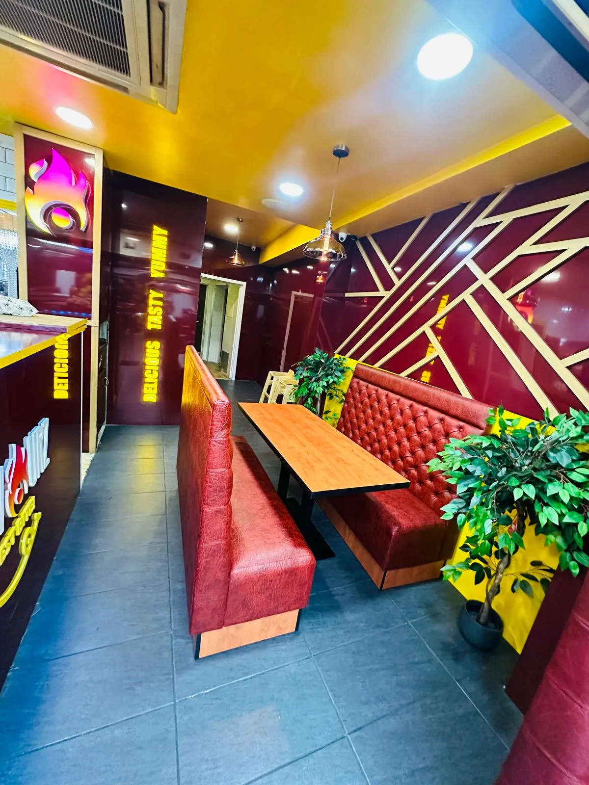 Restaurant interior design with red booth seating, maroon wall panels, gold slat detailing and illuminated wall lettering