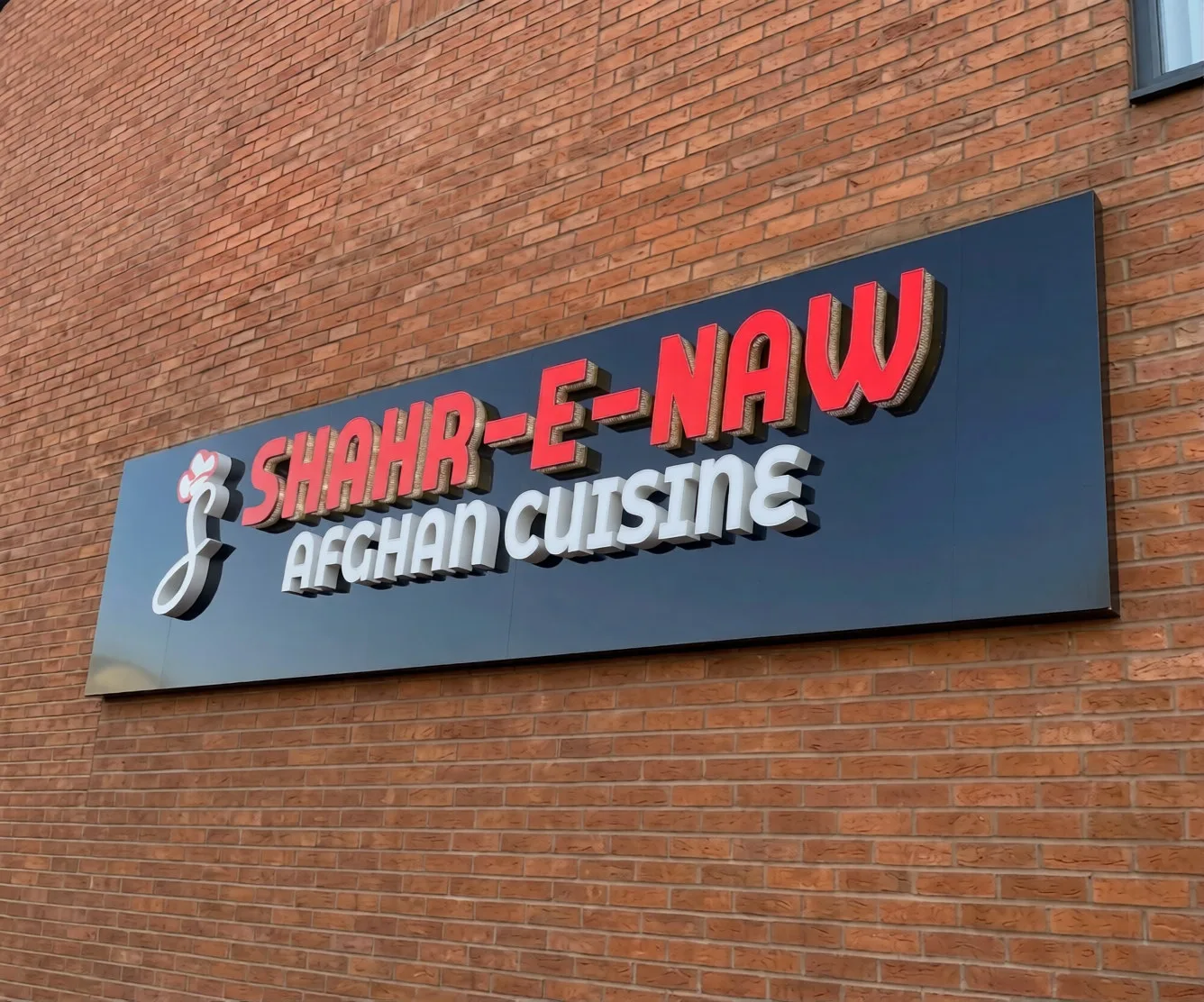 Exterior signage: a large outdoor business sign with raised 3D red and white letters on a dark board fixed to a brick wall