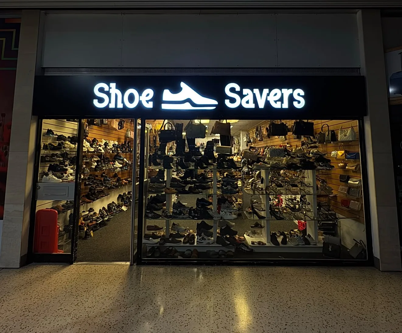 Fret cut shop sign with white cut-out lettering and a shoe logo on a black fascia above a shoe shop window