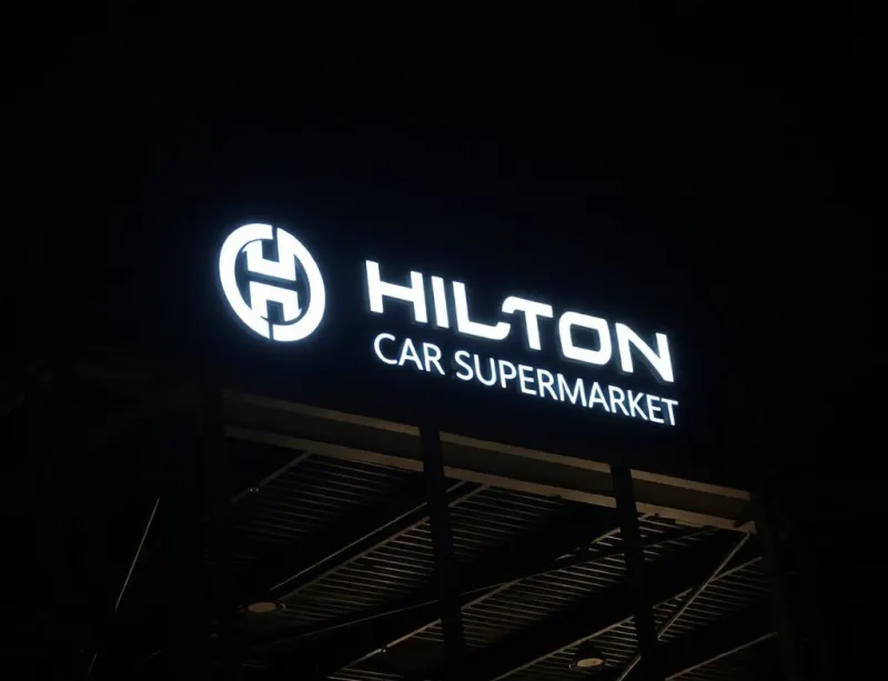 3D illuminated sign with face-lit LED letters and a round logo glowing white on a dark panel above a business at night