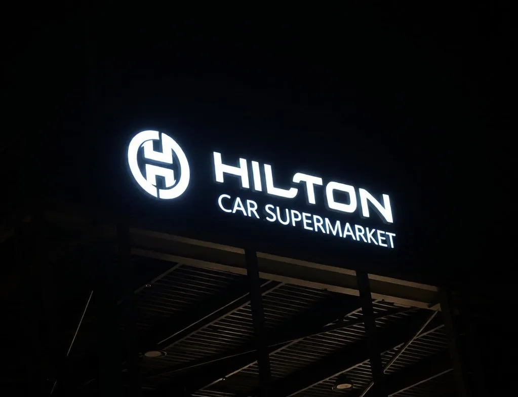 3D illuminated sign with face-lit LED letters and a round logo glowing white on a dark panel above a business at night