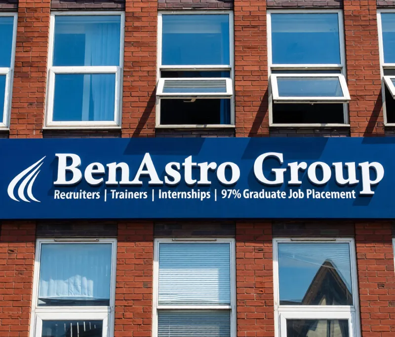 Non illuminated fascia sign with white lettering on a blue board fixed to the front of a brick office building