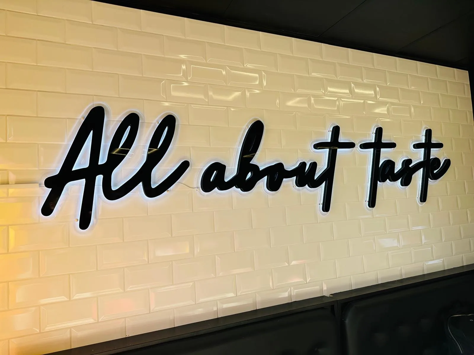 Custom interior wall design featuring black 3D lettering spelling “All about taste” on a cream brick wall.