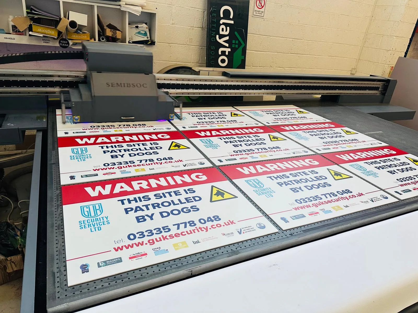 Flatbed printer producing batch custom printed signage warning boards for GUK Security Services Ltd.