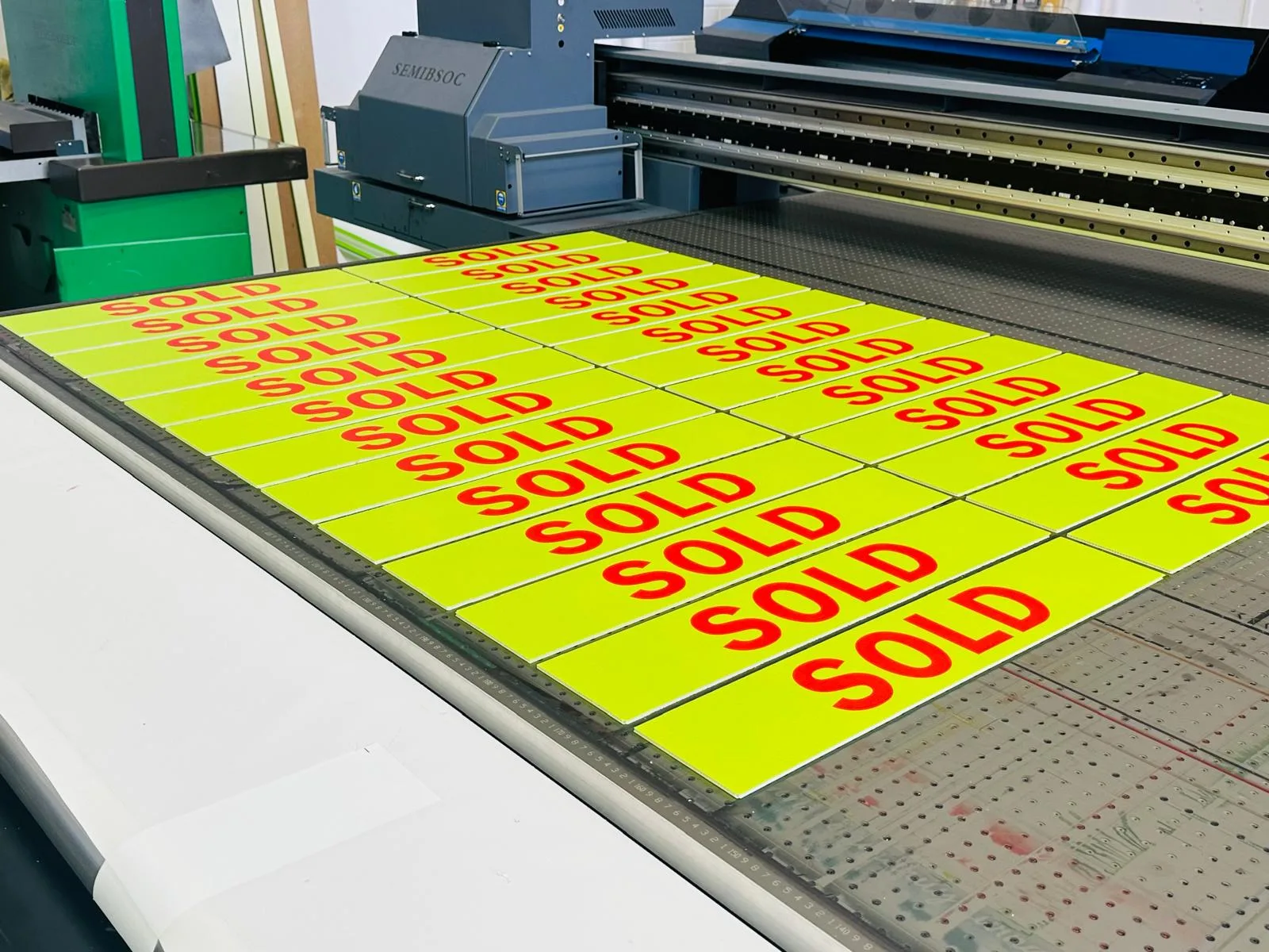 Flatbed printer producing multiple yellow rigid sign printing plates with red SOLD lettering.