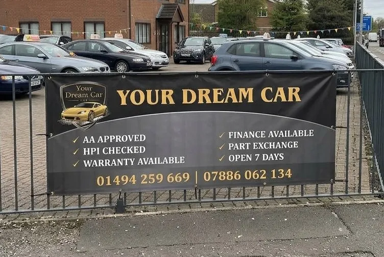 Commercial banner printing: a large black and gold advertising banner fixed to railings on a car dealership forecourt