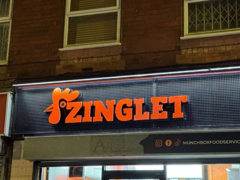 Orange 3D lettering on a shop fascia sign with a dark mesh backing and light strip