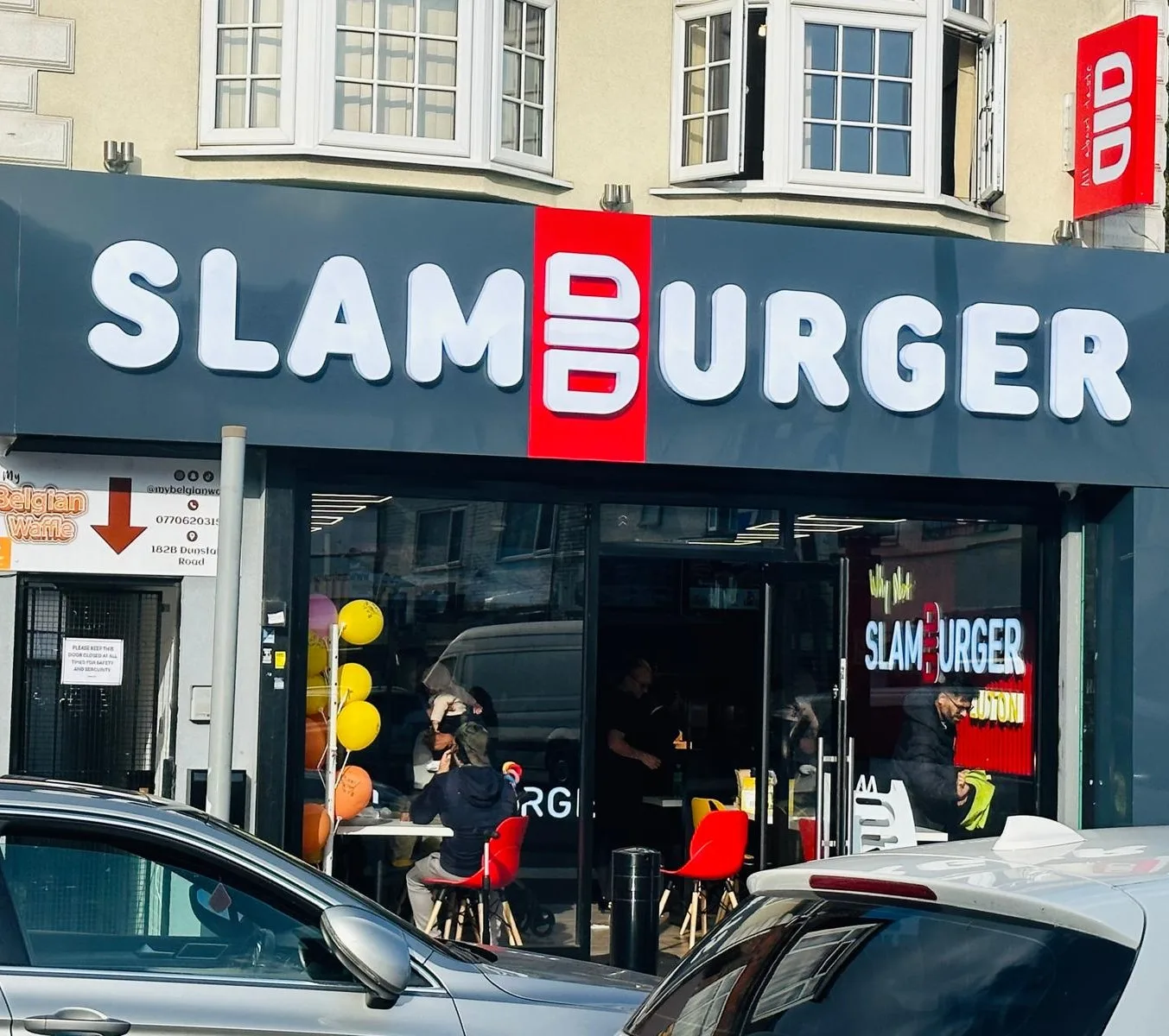 Shop signs on a high street fascia board with large white 3D letters and a red logo panel above a glass shop front