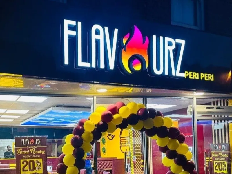 Restaurant shopfront branding with an illuminated fascia sign and logo above a glass entrance decorated with a balloon arch