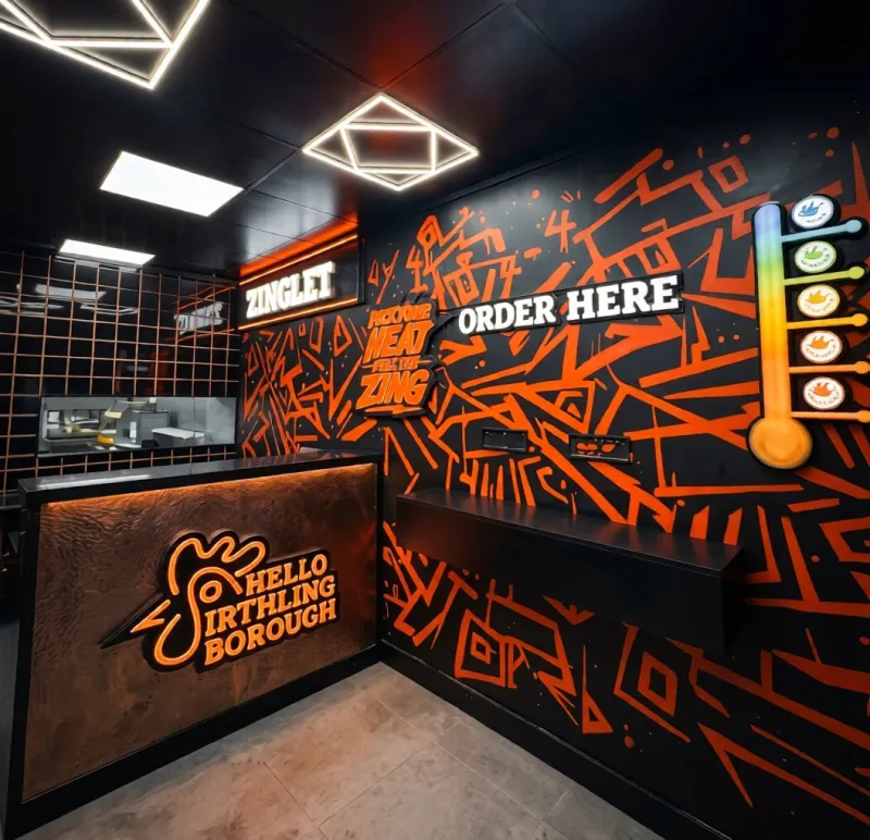Shop branding for a restaurant counter with orange wall graphics, illuminated logo signs and a branded ordering point