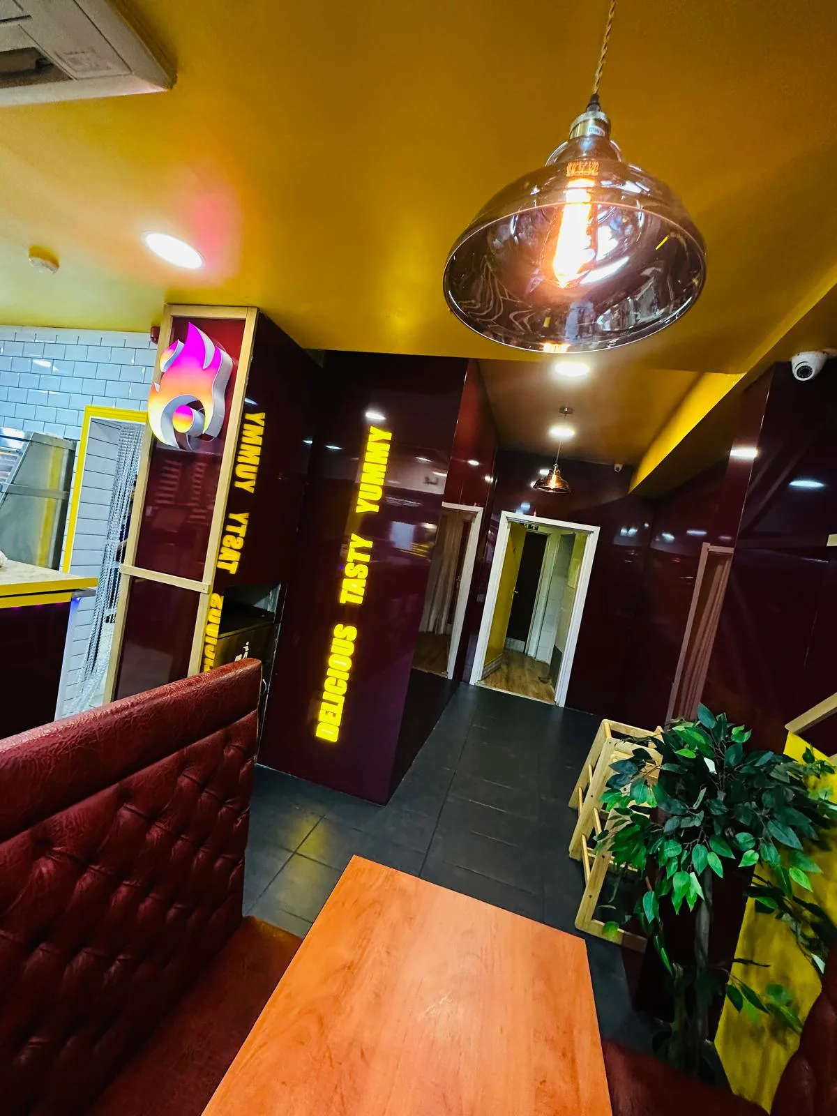 Restaurant interior branding with illuminated yellow lettering and a lit logo on glossy maroon wall panels and booth seating